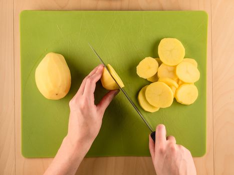 Hands holding knife and slicing potatoe on used plastic board, simple food preparation illustration, vegetarian dieting, top view still life with center composition
