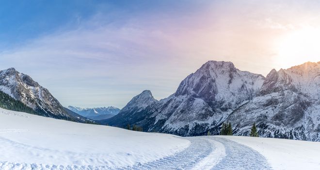 Winter landscape with a road made by a snowmobile, its traces through the layer of snow, in the Austrian Alps mountains, on a sunny day of December.