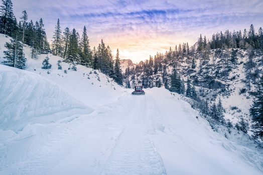 Winter mountain landscape with a road being cleared of snow by a snow grooming machine. Image captured in the Austrian Alps mountains, Ehrwald municipality.