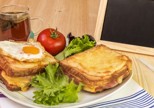 Quick snack with ham and cheese sandwiches, cup of tea, tomato and fresh salad. Beside the plate with food is a blackboard and chalk for writing messages.