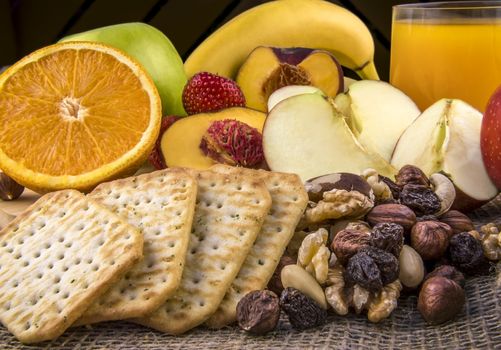 Food photography with a delicious and nutritious meal, formed of fresh fruits, a mix of nuts, salty crackers and a glass of orange juice.