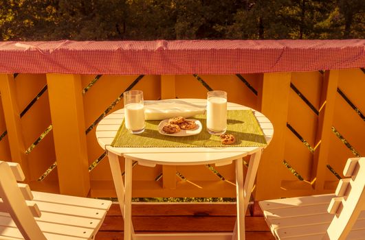 Joyful food photography with a breakfast, cookies and glasses of milk, served on a balcony on a small white table.