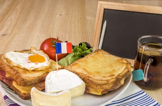 Specific french breakfast with melted cheese sandwiches, white cheese with the french flag, salad, cup of tea  and a blank chalkboard, on a wooden table.