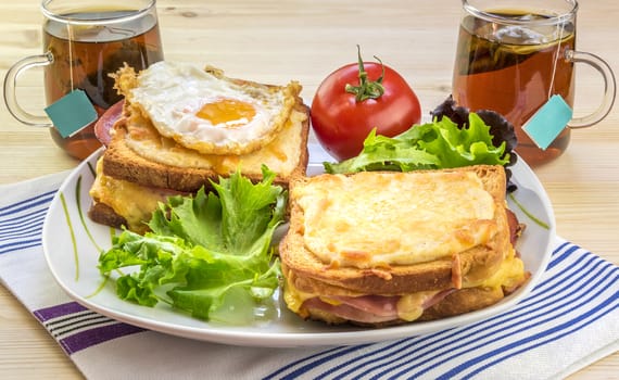 Tasty breakfast for two persons with specific french food, croque madame (with egg) and croque monsieur, seasoned with fresh salad and tea.