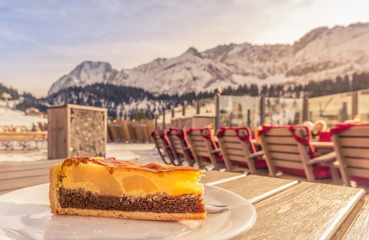 Close-up image with a delicious cake with cocoa batter, vanilla filling and fruits, served on a sunny winter day in the Austrian Alps mountains.