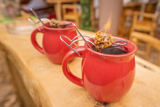 Image with a mug of hot wine, which has tongs with a flaming cone of sugar on top. It is a traditional german drink at Christmas fairs, called "Feuerzangentasse", meaning Fire Cup.