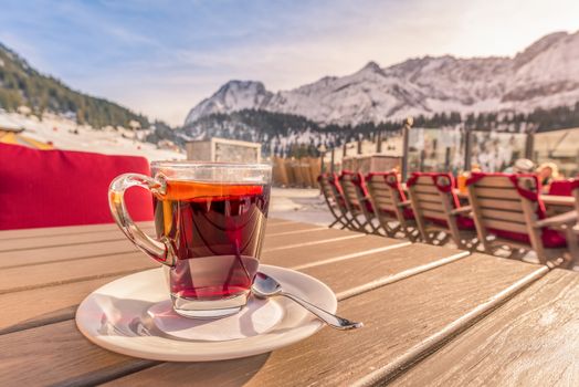 Image with a warm steamy cup of tea, flavored with a slice of orange and served at a mountain restaurant, on a sunny winter day, in Ehrwald, Austria.