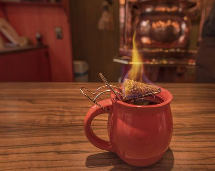 Close-up image with a cup of mulled wine, on top of which stands a burning cone of brown sugar, previously dipped in a lot of rum. This is a traditional german Christmas drink, called "Feuerzangentasse", in translation Fire Cup.