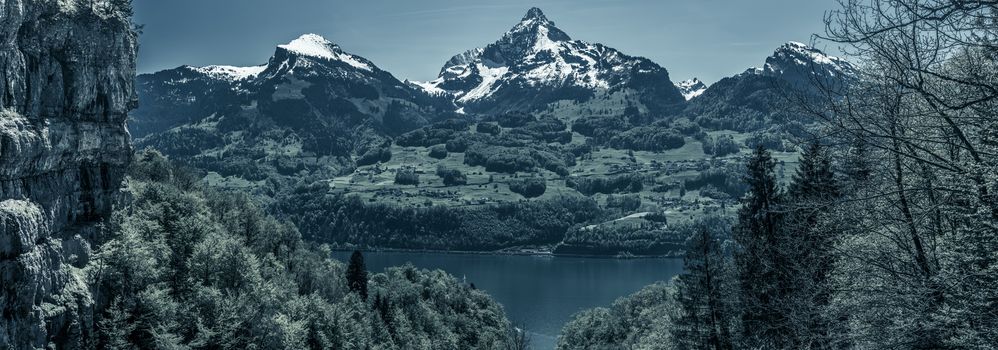 Great panorama over the lake Walensee and its beautiful surroundings, the snowy mountain peaks and huge cliffs, with dark blue colors added. Picture taken near the village Quinten, Switzerland.