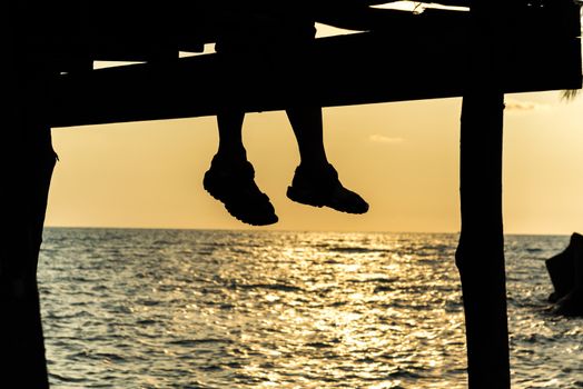 silhouette of feet of couple sitting on the pier at sunset beach,lonely.
