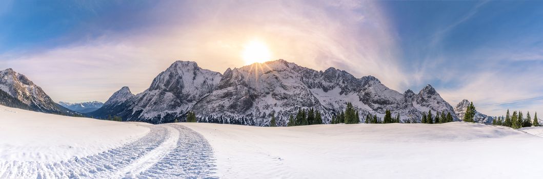 Alpine panorama with the Austrian Alps mountains, from the Ehrwald municipality, the green coniferous trees and a thick layer of snow over its pastures. A gorgeous winter sun overwhelms the entire scene.