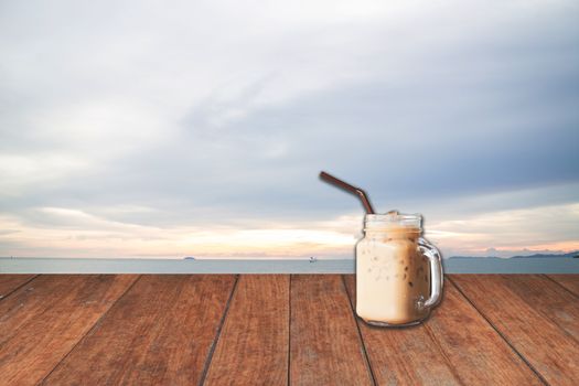 Iced coffee cup with blue sea view and wood floor background