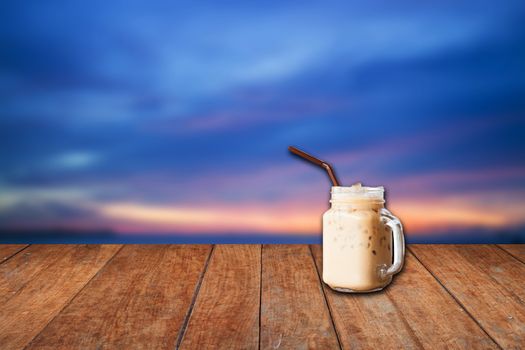 Iced coffee cup with blue sunset sky and wood floor background