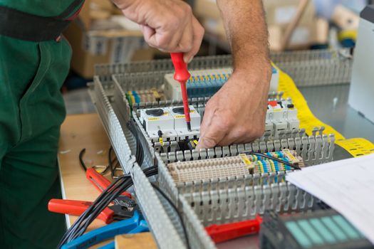 Electrician assembling industrial electric cabinet in workshop.