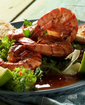 Snack with Big Grilled Shrimps, Fresh Crunchy Greens, Sauces and Roasted Bread Slices on Grey Plate closeup on Wooden background against Light