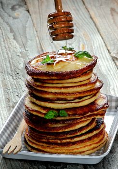 Stack of Delicious Homemade  Pancakes with Mint Leafs and Honey Dripping from Dipper on Checkered Tray closeup on Wooden background