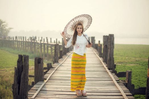 The beautiful Burmese woman in Myanmar traditional costume,with umbrella walking on Ubein bridge, Mandalay Myanmar 