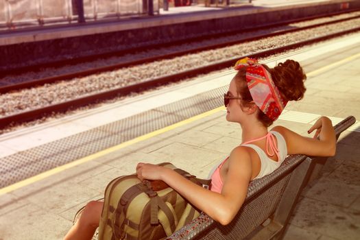Young sexy woman backpacker sitting on bench on railway station. Travel concept.
