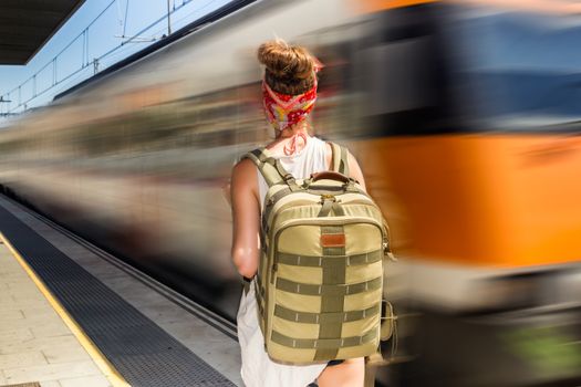 Young sexy woman backpacker waiting for train on platform on railway station. Travel concept.