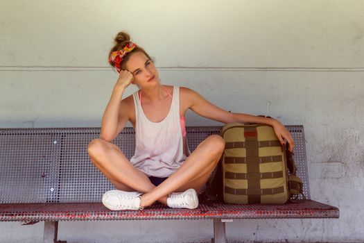 Young sexy woman backpacker sitting on bench on railway station.Travel concept.