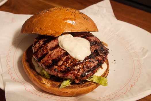 Fresh burger with beef and pork and special sauce closeup on wooden table.