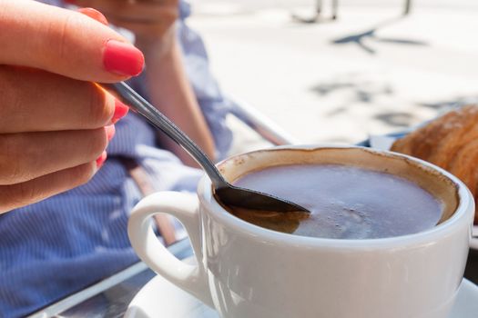 woman hand lower the spoon into the cup of coffee close up outdoor