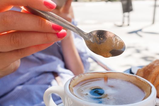 woman hand lower the spoon into the cup of coffee close up outdoor