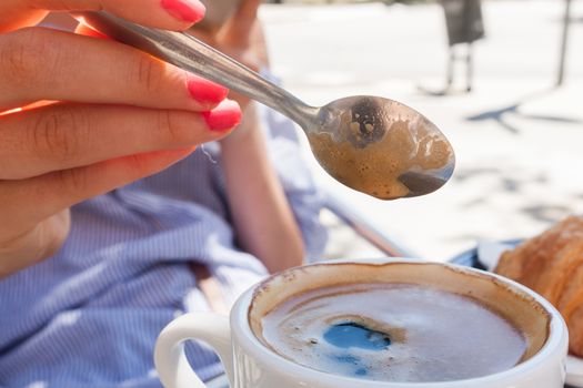 woman hand lower the spoon into the cup of coffee close up outdoor