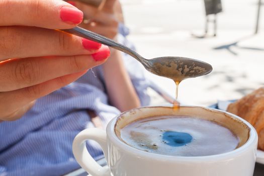 woman hand lower the spoon into the cup of coffee close up outdoor