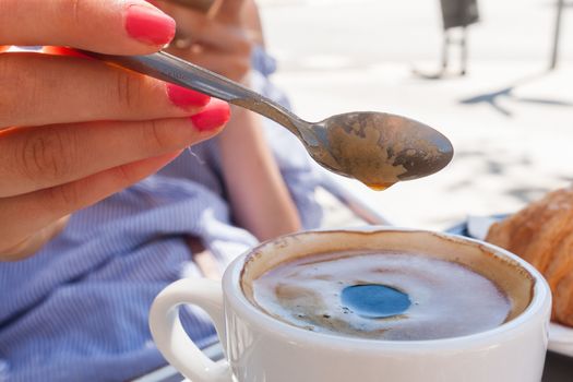 woman hand lower the spoon into the cup of coffee close up outdoor