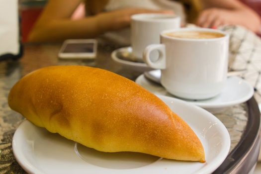 fresh bun on plate with coffee cup on cafe table with blurred woman on backgound