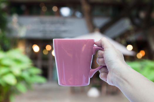 Woman hand holding coffee mug with cafe blurred abstract background