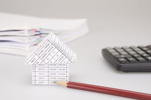 House and brown pencil have blur black calculator and pile of paperwork with colorful paperclip on white background.