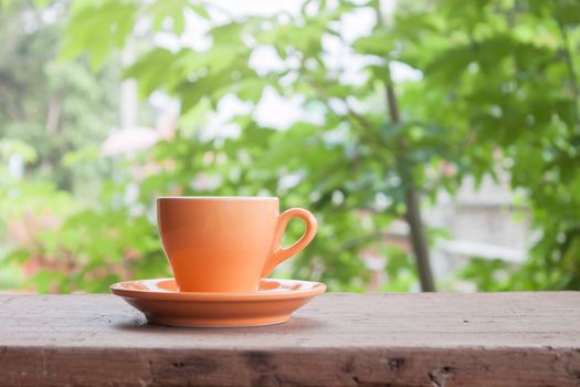 Orange coffee cup on tabletop with blurred green leaves background