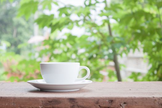 White coffee cup on tabletop with blurred green leaves background