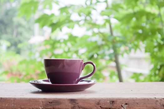 Purple coffee cup on tabletop with blurred green leaves background