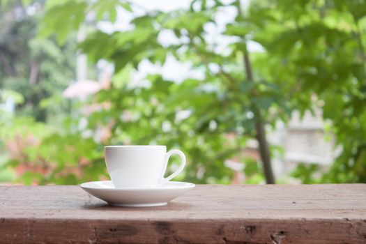 Mini white coffee cup on tabletop with blurred green leaves background