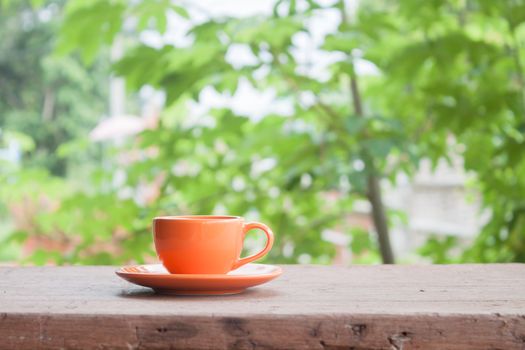 Mini orange coffee cup on tabletop with blurred green leaves background