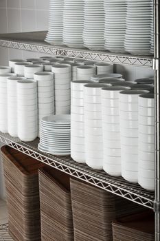 stacks of many white plates on a wire rack shelf in a commercial kitchen