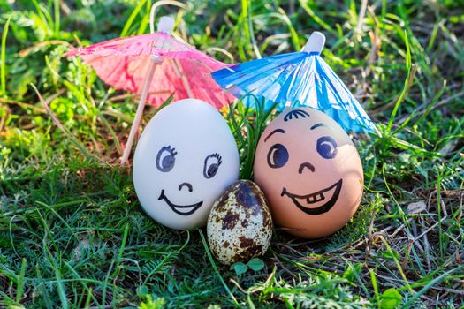 Funny eggs imitating happy smiling mixed couple white and colored parents with versicolored baby under umbrella