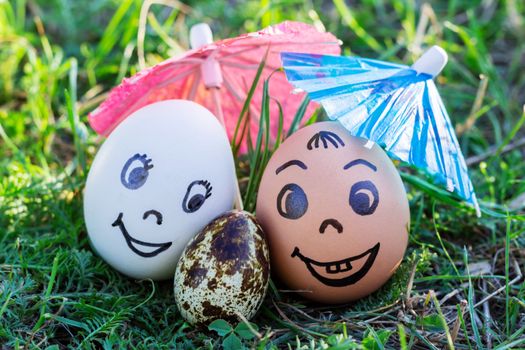 Funny eggs imitating happy smiling mixed couple white and colored parents with versicolored baby under umbrella