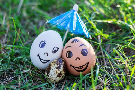 Funny eggs imitating happy smiling mixed couple white and colored parents with versicolored baby under umbrella