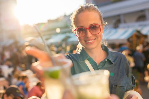 Beautiful young girl toasting outdoors on Open kitchen street food festival in Ljubljana, Slovenia. Popular summer urban tourist event in capital.