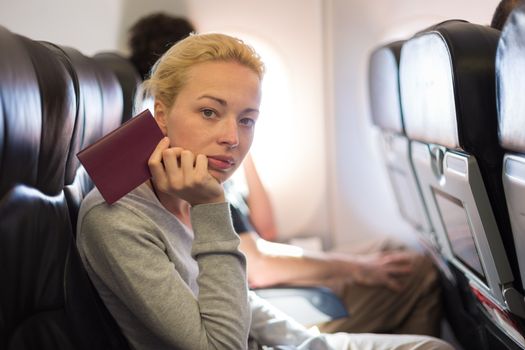 Woman flying by commercial airplane, sitting on her seat, holding passport in her hand, waiting to arrive at immigration point.