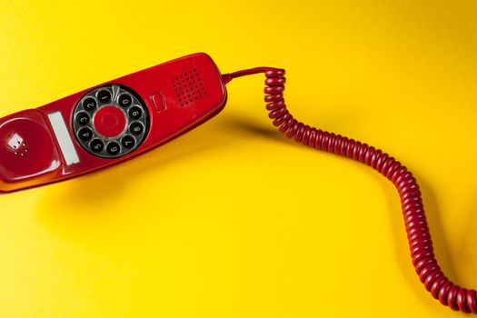 Old red phone off the hook on yellow background