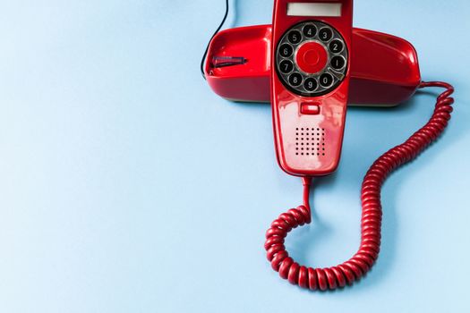 Old red phone off the hook on blue background