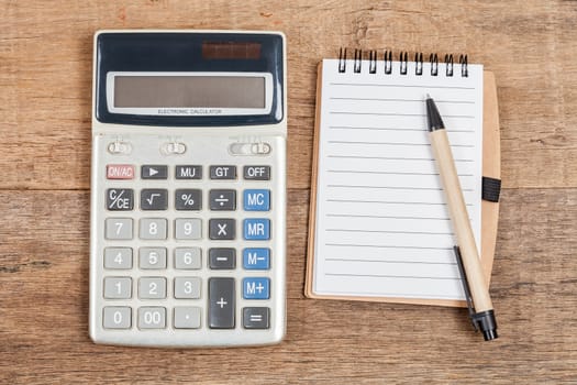 notebook showing empty page  and calculator on wooden desk