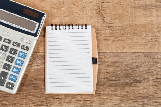 notebook showing empty page  and calculator on wooden desk
