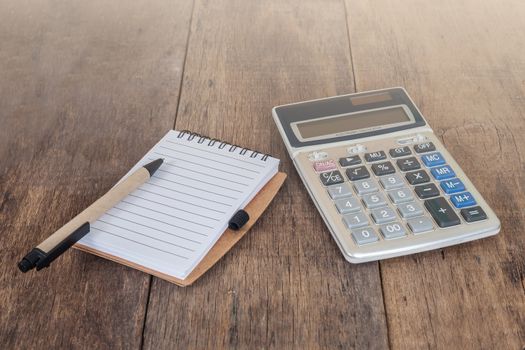 notebook showing empty page  and calculator on wooden 
desk