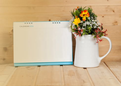 Blank calendar with cup and vase on wood table with yellow light tone